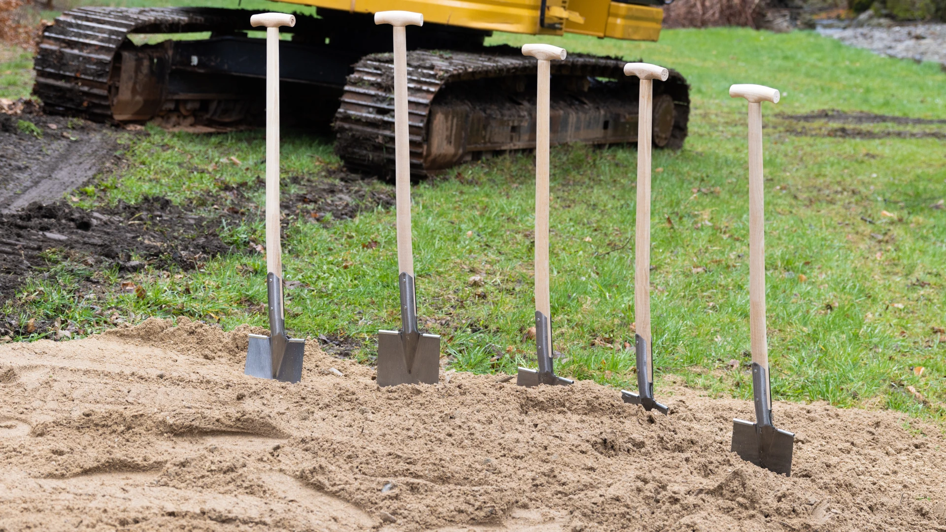 Bester günstiger Spaten unter 30 € für den Garten 2025 – Mein Test mit Empfehlungen 4 Bester Spaten Garten – sechs Holzspaten im Sand vor gelbem Bagger