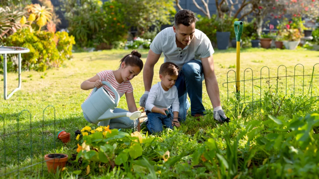Durch Gärtnern zur Achtsamkeit – Vater gärtnert mit zwei Kindern und gießt gemeinsam Blumen im Familiengarten