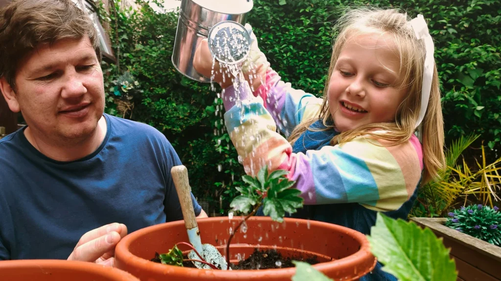 Durch Gärtnern zur Achtsamkeit – Vater und Tochter gießen zusammen eine Pflanze im Blumentopf